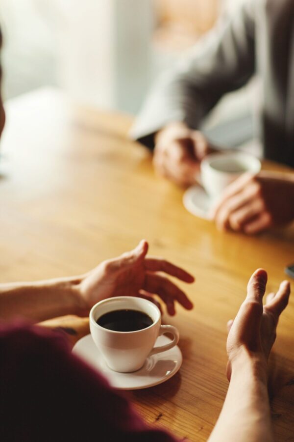 Hände von zwei nicht erkennbaren Geschäftsleuten, die Geschäftsgespräche über Kaffee führen und im Café am Tisch sitzen